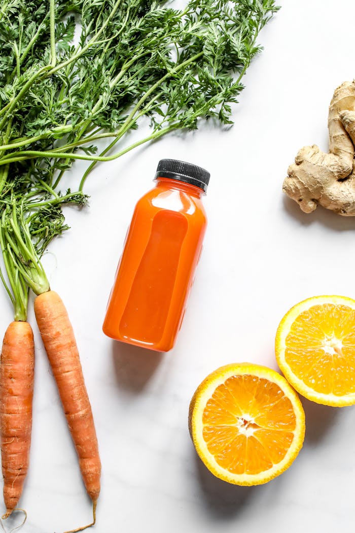 pexels-photo-4443444 Vibrant orange juice bottle surrounded by fresh carrots, orange slices, and ginger.